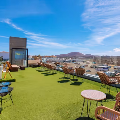 Terraza superior con césped artificial, sillones de mimbre y vistas lejanas a las montañas de Fuerteventura.