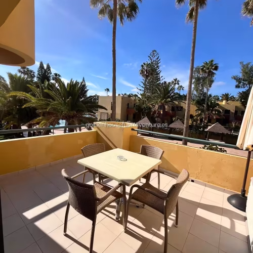 Terraza privada con mesa, cuatro sillas y vistas a zona residencial con palmeras.