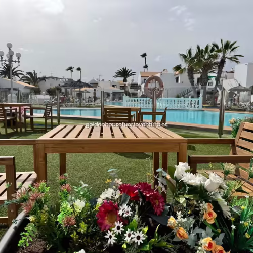 Mesa de madera exterior con flores en primer plano y vistas a la piscina del complejo.