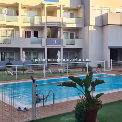 Piscina con valla de seguridad blanca y edificios de apartamentos al fondo.