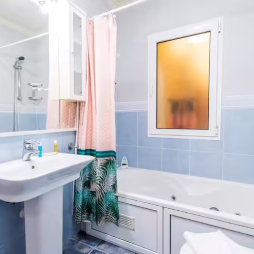 Baño con azulejos azules, bañera con mampara de cortina y lavabo de pie en Villa Sophia.