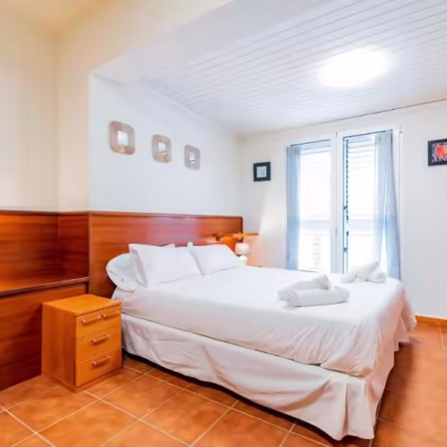 Dormitorio con cama doble, mesilla de noche y ventana con persianas en Caleta de Fuste.