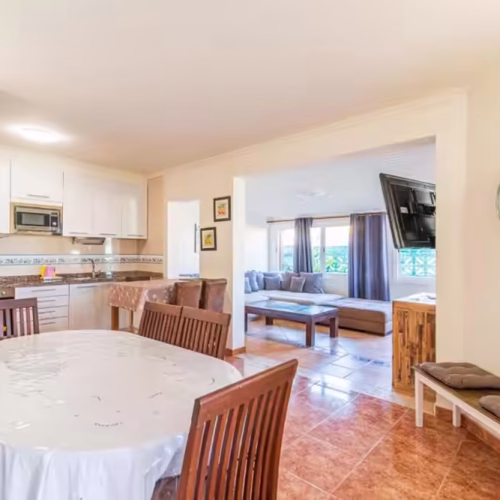 Zona de comedor con mesa amplia y vista al salón con televisión y sofá en Fuerteventura.