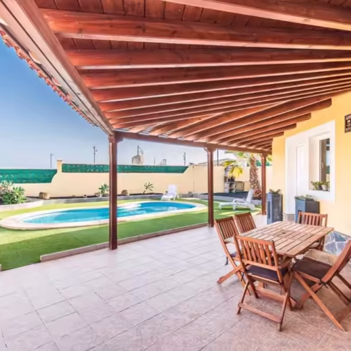 Porche cubierto con estructura de madera, mesa de comedor exterior y vistas a la piscina.
