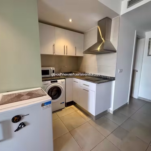 Vista de la cocina con nevera pequeña en primer plano y pasillo hacia otras estancias.