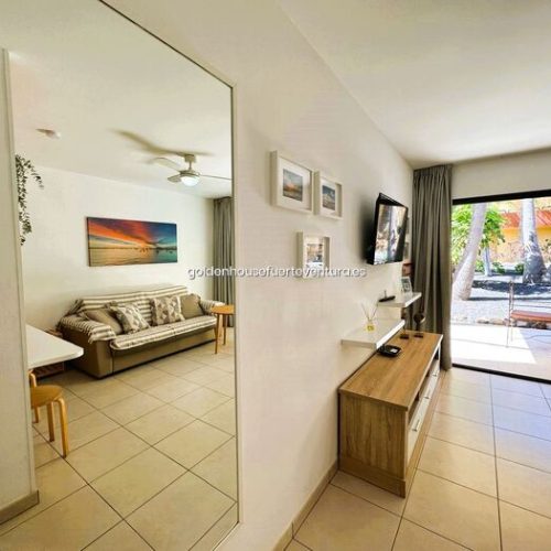 Salón con televisión, mueble de madera, espejo grande y salida directa a la terraza.