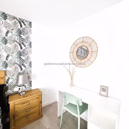 Escritorio blanco con silla verde menta y espejo redondo de mimbre en dormitorio.