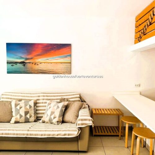 Sofá a rayas frente a barra blanca con taburetes de madera y estante decorativo superior.