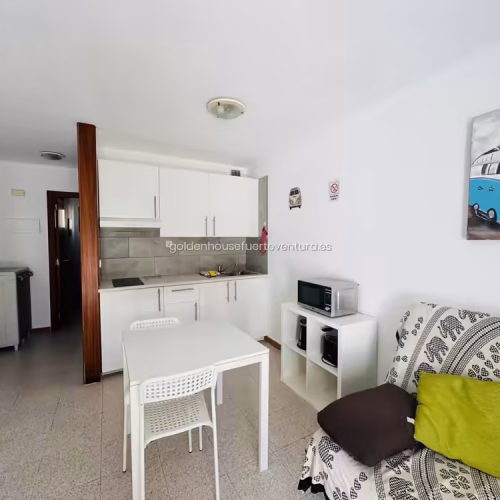 Espacio abierto que integra la cocina blanca, mesa de comedor y parte del salón.