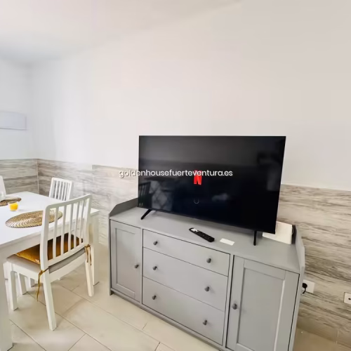 Comedor interior con detalles de fibras naturales y Smart TV en mueble aparador gris.