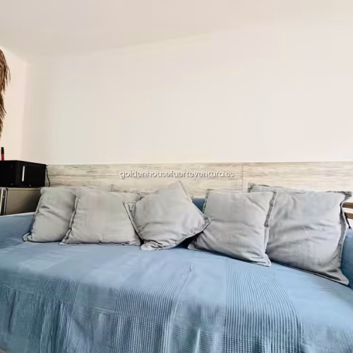 Sofá azul con cojines grises y decoración de pared en alojamiento de Fuerteventura