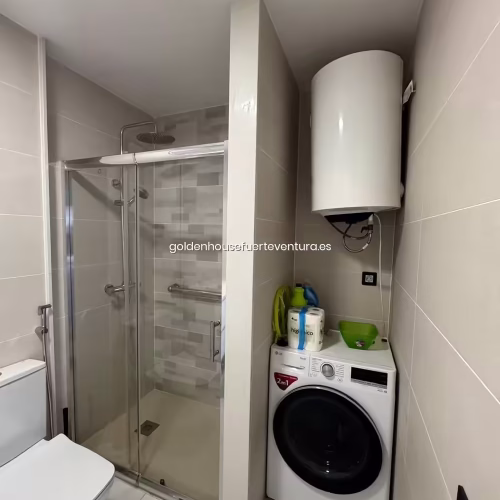 Lavadora de carga frontal instalada en el baño bajo el termo eléctrico de agua.