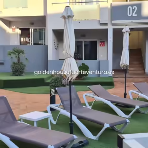 Hamacas grises y sombrillas dispuestas sobre césped artificial junto a la piscina.